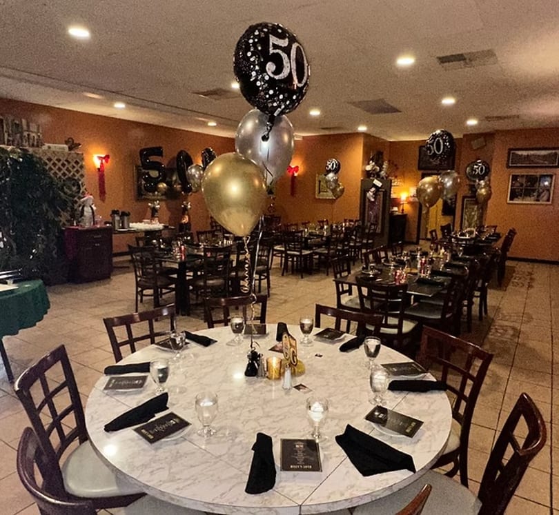 Restaurant dining room decorated with black, gold, and silver "50" balloons for a celebration.