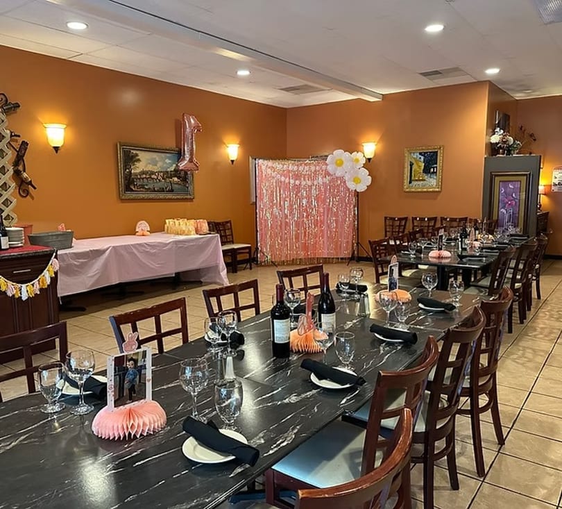 Restaurant dining room set up for a birthday party with long tables, decorations, and a pink backdrop.