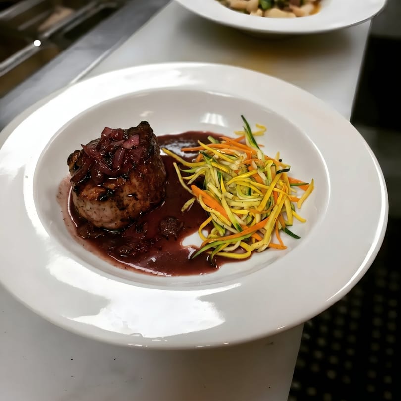 Seared pork tenderloin with red wine reduction and julienned zucchini and carrots on a white plate.