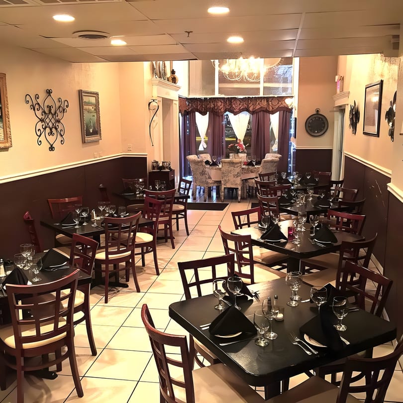 Empty restaurant dining room with dark tables, wooden chairs, and elegant decor.