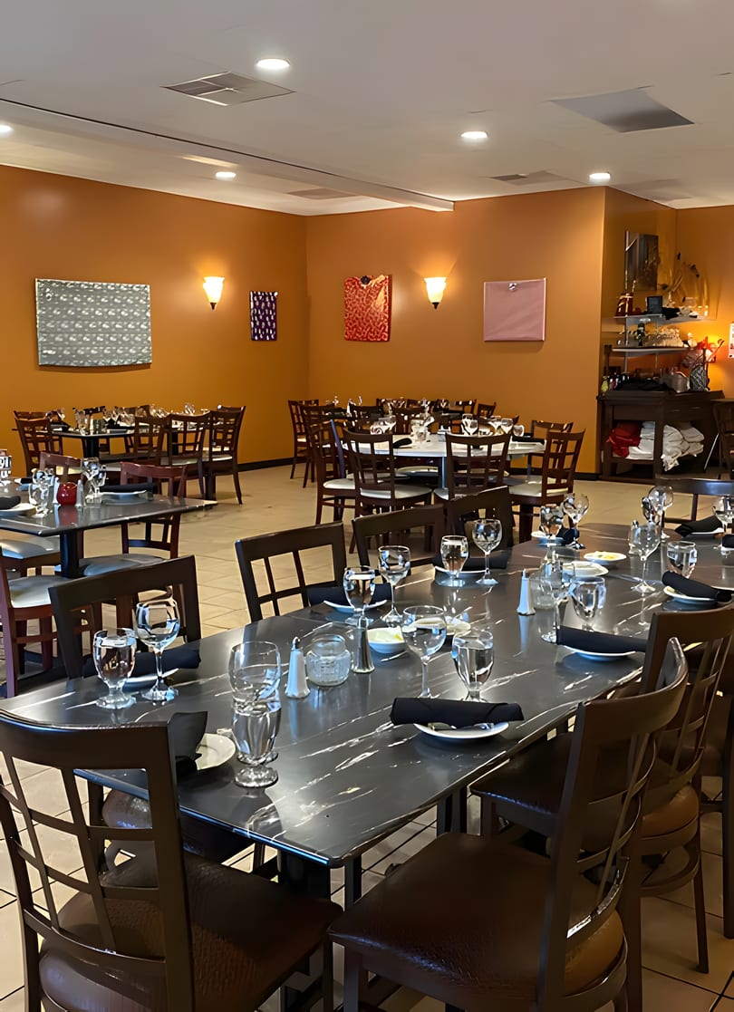 Restaurant dining room with multiple tables set with glasses and black napkins, orange walls, and modern art.