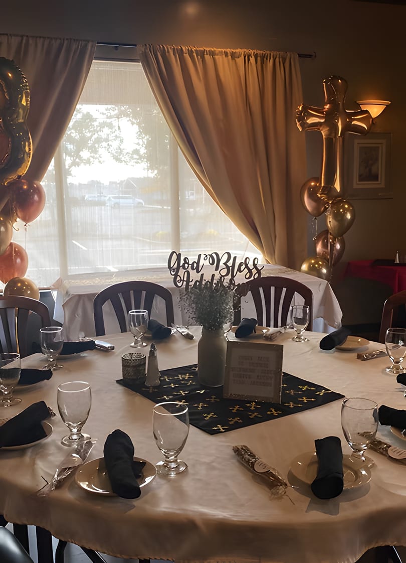 A decorated table with a "God Bless" sign, balloons, and place settings for a special event.