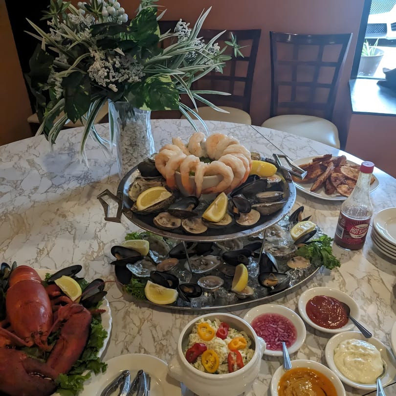 A lavish seafood tower with shrimp, oysters, mussels, clams, lobster, and various sauces on a marble table.